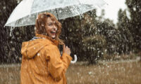 Cheerful pretty girl holding umbrella while strolling outside. She is turning back and looking at camera with true delight and sincere smile. Copy space in right side